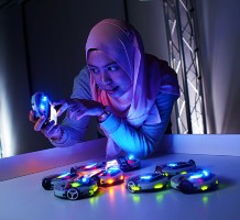 Female research student in the robot lab operating small robots with brightly coloured lights.